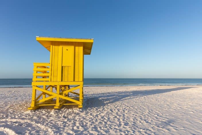 yellow life guard stand on a white beach with blue water and skies, siesta key