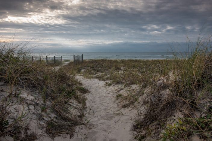 a walkway through the dunes on st. george beach with sea grass and dark skies