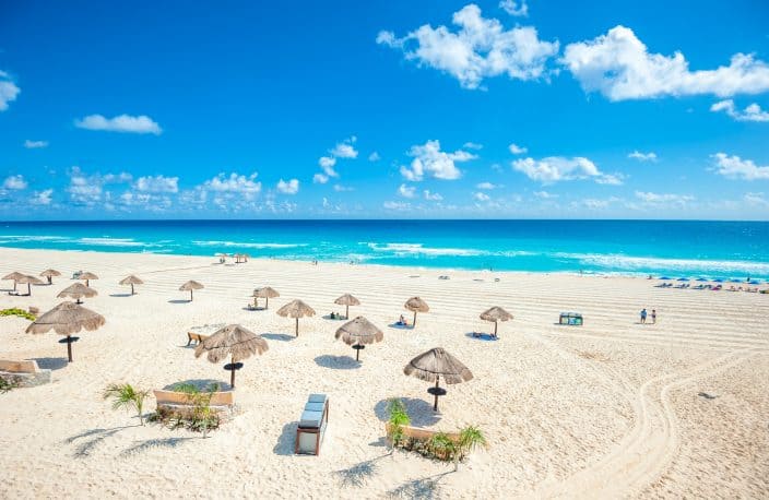 a panorama of Cancun Beach with umbrellas, golden sand, blue water, and skies