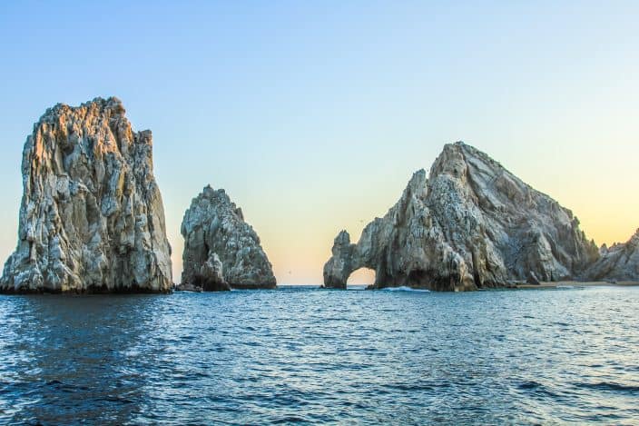 Los Arcos arch rock formation with a sunset sky and reflective water at Lands End in Cabo San Lucas, Mexico.