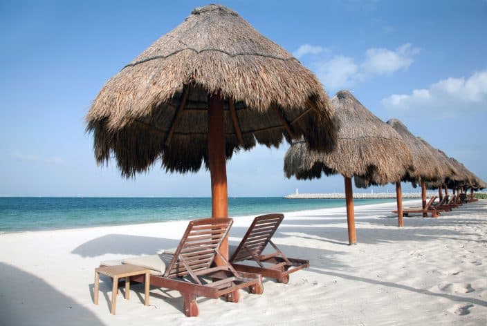 Playa Del Carmen beach in Mexico with palm umbrellas, beach chairs, blue water and skies, and golden sand
