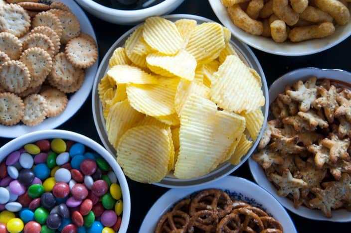 an assortment of snacks in different bowls including MnMs, pretzels, crackers, potato chips and cheese puffs