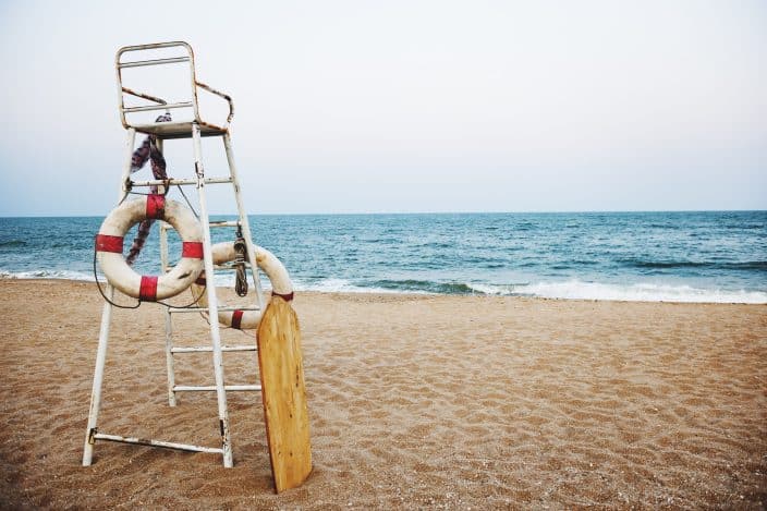 view of the tall lifeguard chair in front of the seashore with golden sand and grey blue skies to represent a useful beach hack