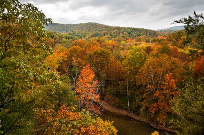 Buffalo National River in Arkansas with orange, red, and yellow leaves on the trees and grey skies, a fall bucket list destination