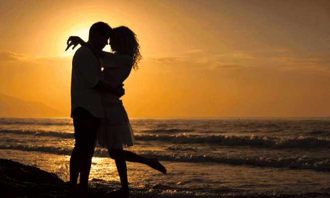 couple hugging and kissing at sunset on the beach with the ocean in the background