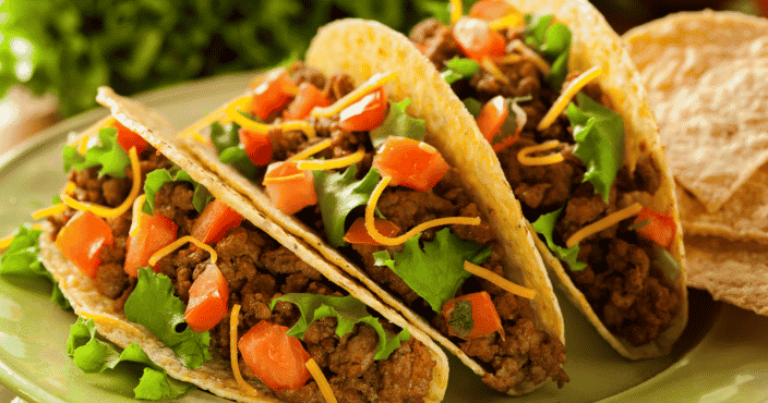 Tacos with ground beef, lettuce and tomato in a hard shell on a plate
