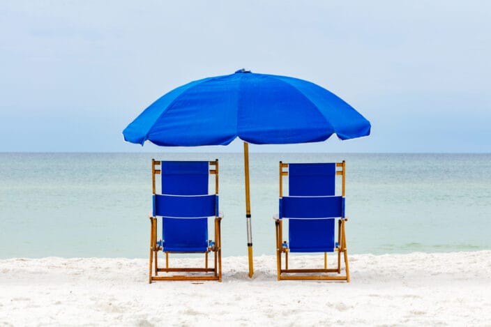 blue beach chairs on white sand facing the light turquoise water of the Gulf of Mexico