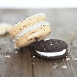 Oreo macaroon and an oreo cookie on a wood plank table with crumbs