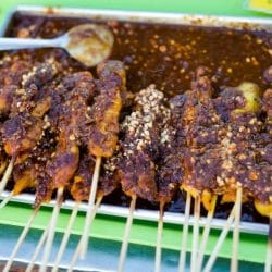 spicy chicken satay skewers on a metal tray on a green plate