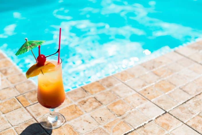 mai tai cocktail with a festive umbrella, orange slice, and cherry on tile by the pool