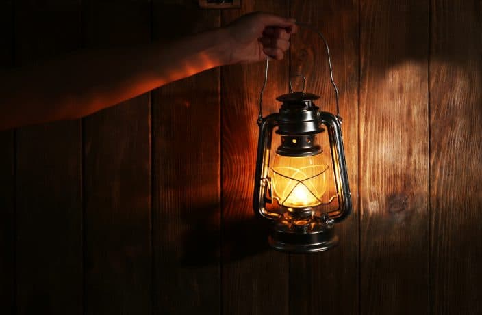 a lit lantern being held up by a hand in front of a wooden background