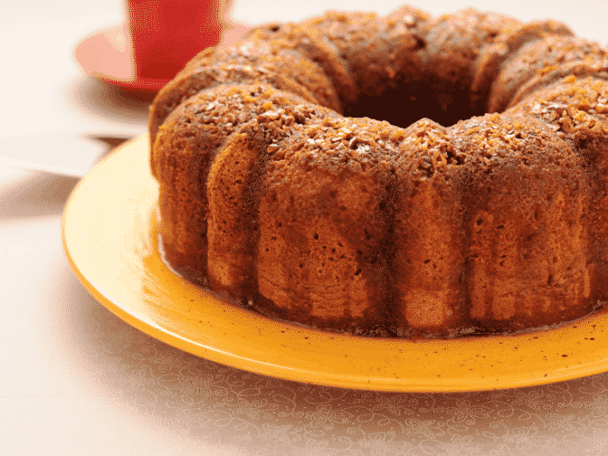 a rum cake sitting on a yellow plate on a beige counter top with a red cup in the background