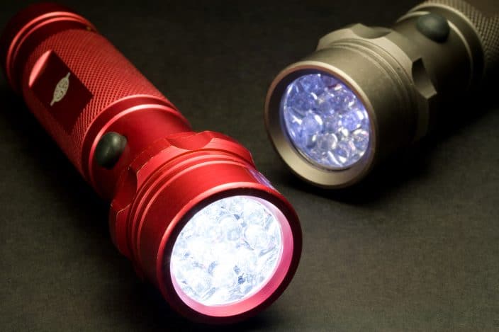 a red and a gold flashlight that are on laying on a dark background, to represent an important camping essential