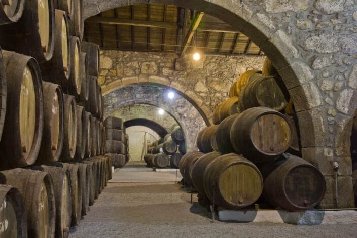 old cellar with rows of wooden wine barrels stacked on top of each other with grey arches made of stone in a Georgia Winery