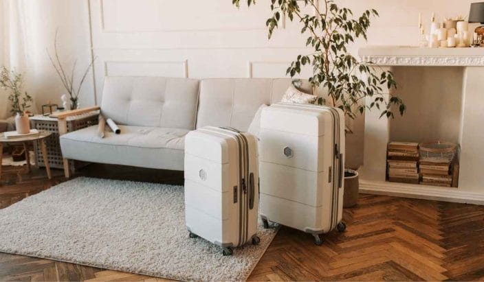two white suitcases standing in a living room with a white sofa, wood floors, a white rug, green plant and cabinet to represent  summer packing list hacks