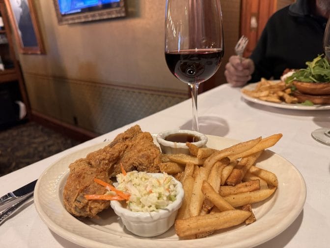 fried chicken on a white platter, on a white cloth with a glass of red wine